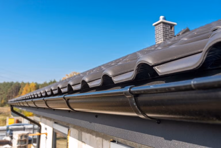 What is the Lifespan of a Commercial Roof? - The edge of a dark charcoal metal roofing system with a matching dark charcoal metal gutter system.